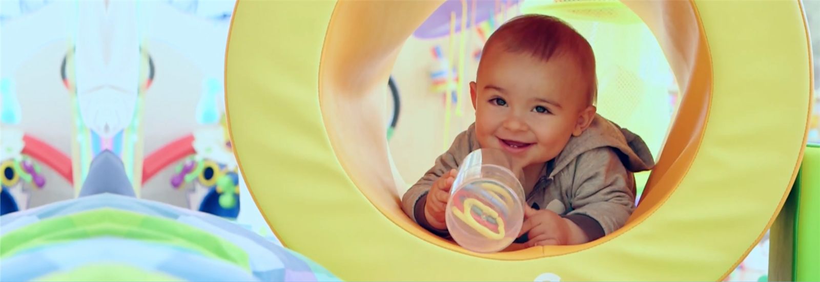Smiling baby playing inside a soft play tunnel at the school